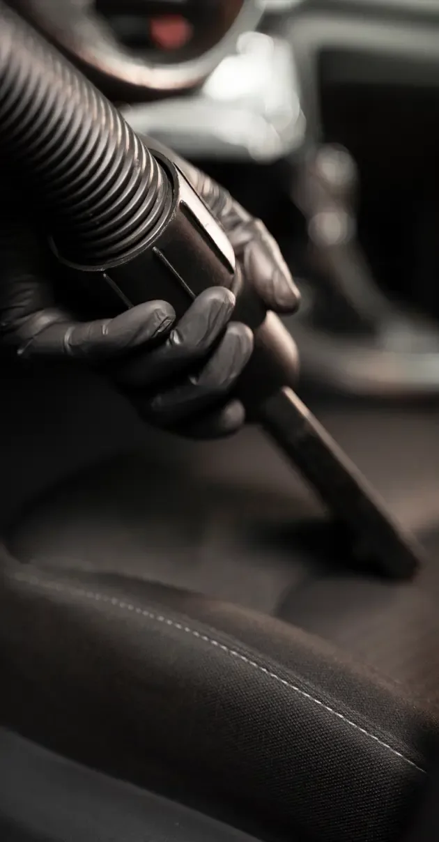 Gloved hand vacuuming a cloth car seat