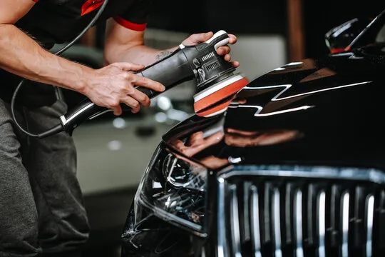 Dual-action polisher working the hood of a black car