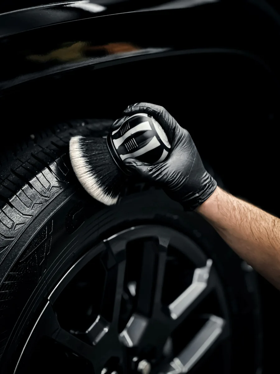 Gloved hand brushing a tire sidewall on a black car